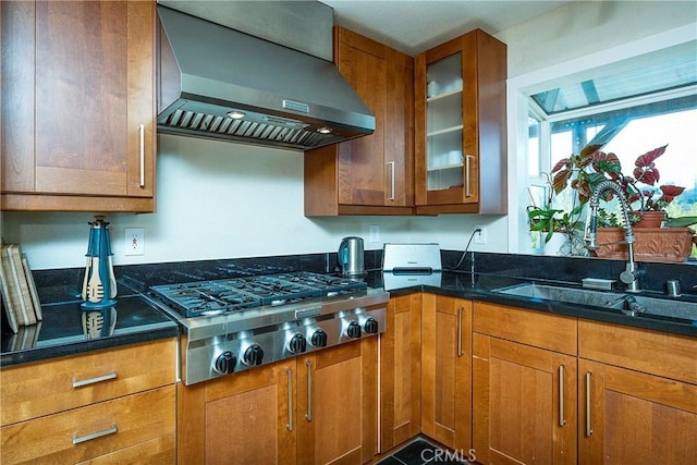 kitchen with dark stone countertops, sink, wall chimney range hood, and stainless steel gas cooktop