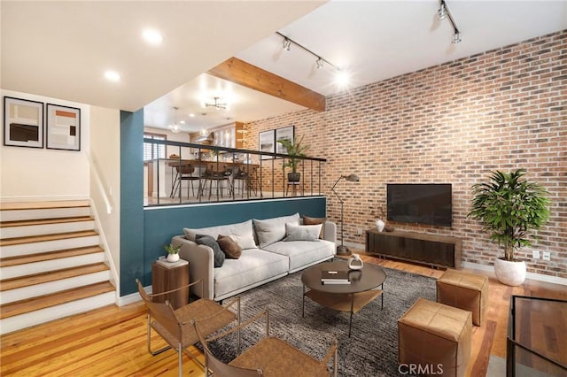 living room featuring beamed ceiling, wood-type flooring, brick wall, and track lighting