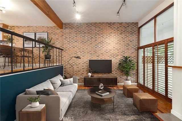 living room with hardwood / wood-style flooring, beamed ceiling, brick wall, and track lighting