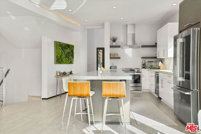 kitchen with appliances with stainless steel finishes, white cabinetry, a kitchen island, and wall chimney range hood