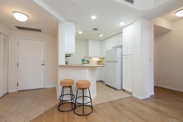 kitchen featuring kitchen peninsula, a kitchen breakfast bar, white fridge, and white cabinetry