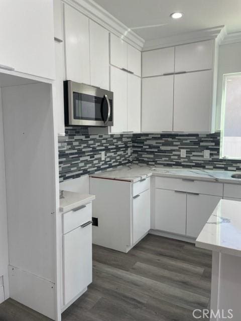 kitchen featuring tasteful backsplash, white cabinetry, dark wood-type flooring, and ornamental molding