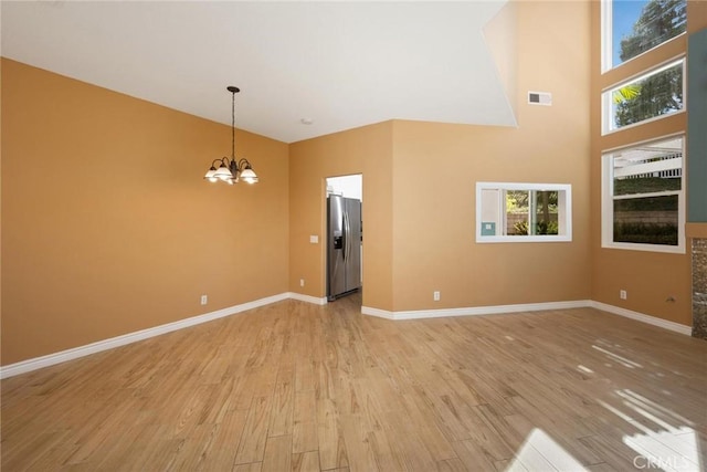 unfurnished living room with a high ceiling, a healthy amount of sunlight, a notable chandelier, and light hardwood / wood-style floors