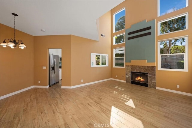 unfurnished living room with a chandelier, a high ceiling, light hardwood / wood-style floors, and a fireplace