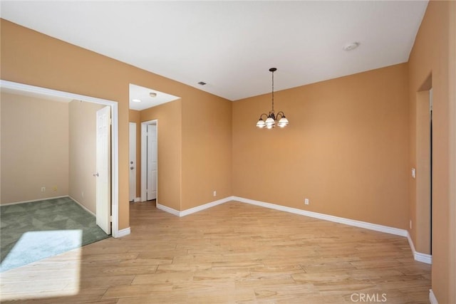 spare room with a notable chandelier and light wood-type flooring