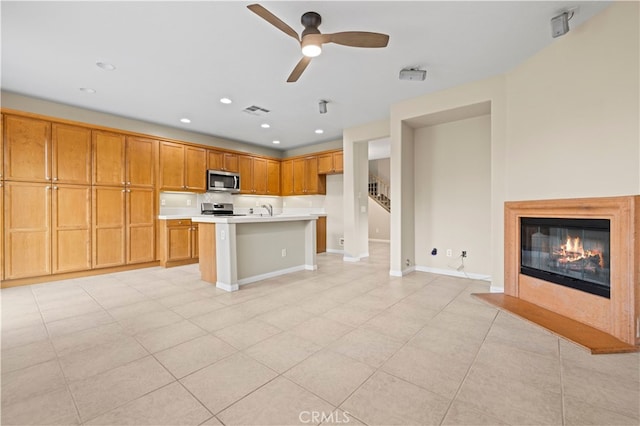 kitchen featuring appliances with stainless steel finishes, a center island with sink, light tile patterned floors, and ceiling fan