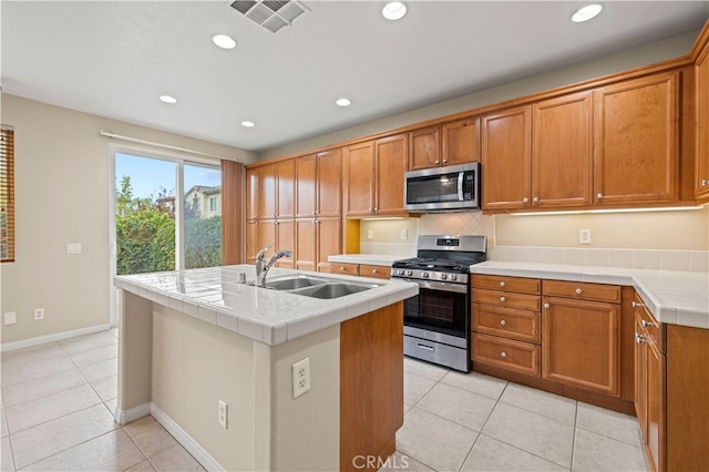 kitchen featuring appliances with stainless steel finishes, sink, light tile patterned floors, tile countertops, and a center island with sink