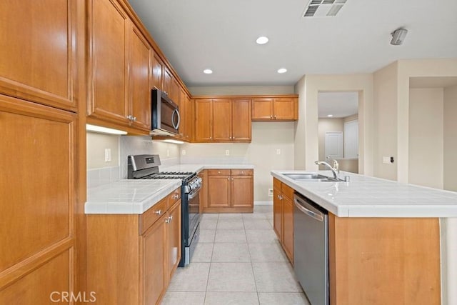 kitchen featuring tile countertops, a center island with sink, sink, light tile patterned floors, and appliances with stainless steel finishes