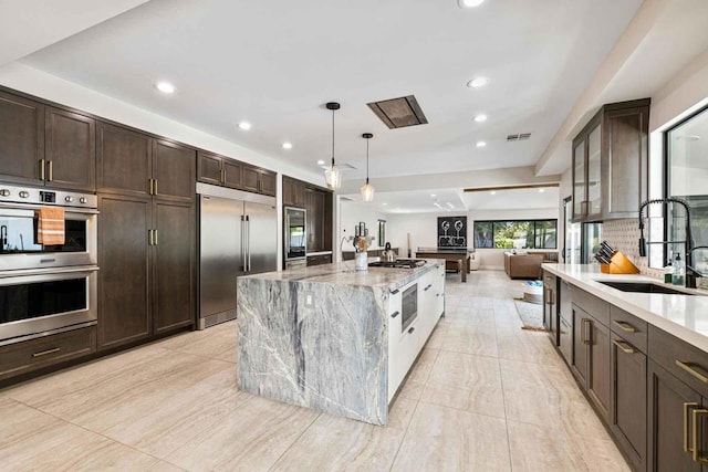 kitchen featuring light stone countertops, appliances with stainless steel finishes, sink, a large island with sink, and pendant lighting