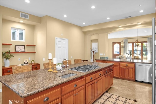 kitchen with an inviting chandelier, appliances with stainless steel finishes, a kitchen island with sink, hanging light fixtures, and sink