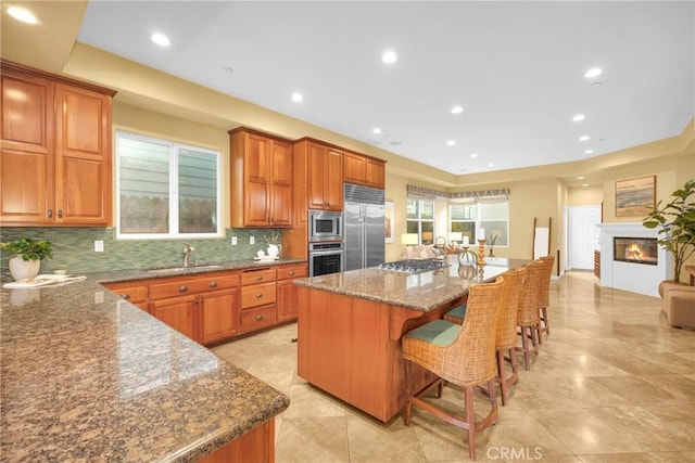 kitchen with a breakfast bar area, a center island, stone countertops, built in appliances, and sink