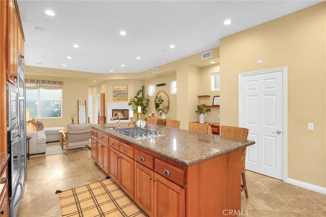 kitchen with light tile patterned floors, a kitchen bar, appliances with stainless steel finishes, dark stone counters, and a center island