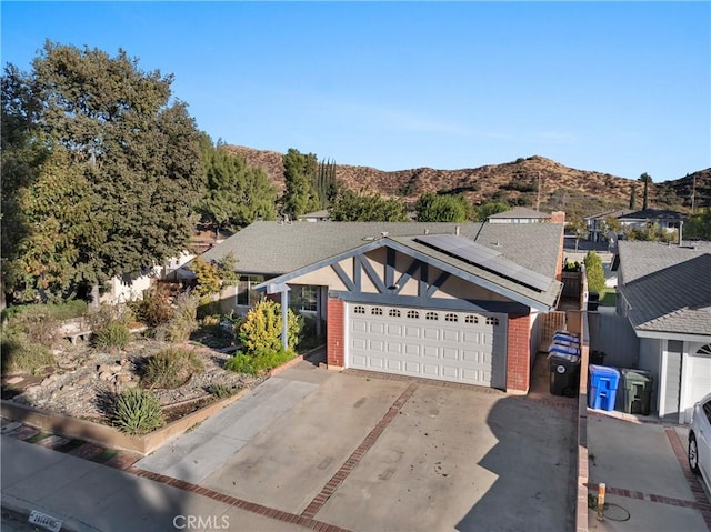 ranch-style house featuring an attached garage, a mountain view, solar panels, brick siding, and driveway