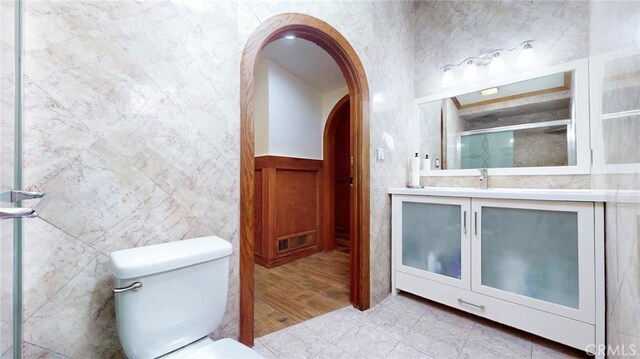 full bath with visible vents, a wainscoted wall, toilet, a shower with door, and vanity