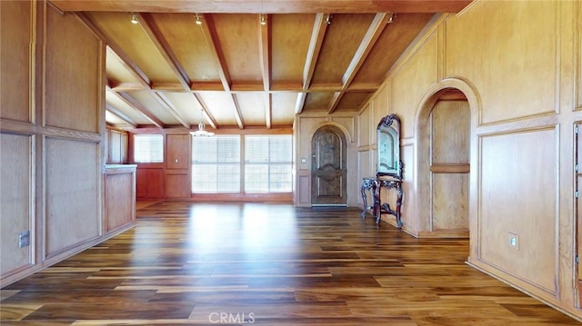 interior space featuring beam ceiling, wooden walls, dark wood-style flooring, and a decorative wall