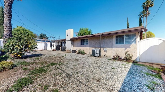 rear view of house featuring a gate, fence, central AC, a chimney, and stucco siding