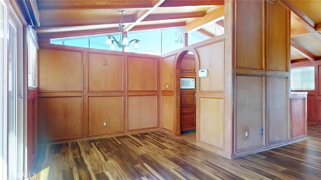 kitchen with arched walkways, a decorative wall, vaulted ceiling with beams, and wood finished floors