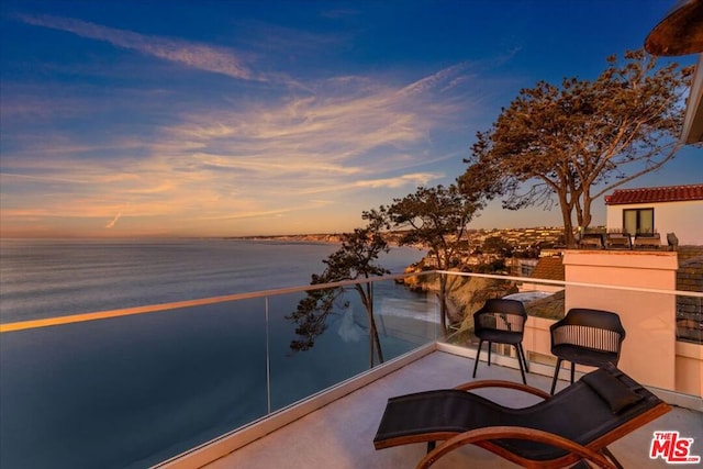 balcony at dusk featuring a water view