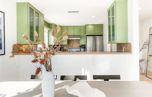 kitchen featuring green cabinetry, light tile patterned floors, appliances with stainless steel finishes, tasteful backsplash, and kitchen peninsula