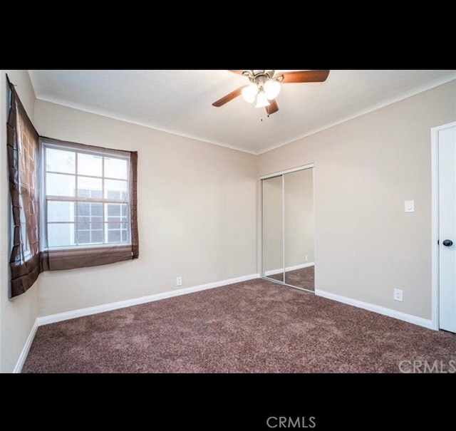 unfurnished bedroom with ceiling fan, a closet, and dark colored carpet