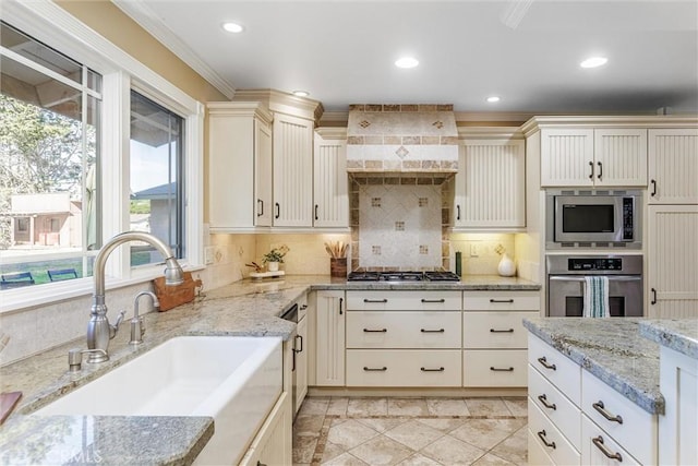 kitchen featuring backsplash, light stone counters, ornamental molding, stainless steel appliances, and sink