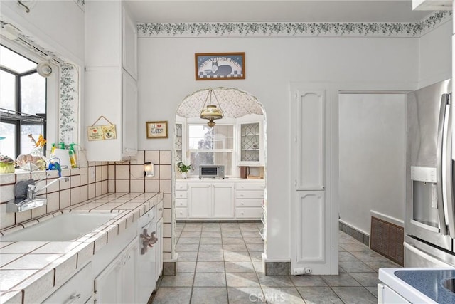 kitchen featuring white cabinetry, sink, stainless steel fridge, tile counters, and light tile patterned floors