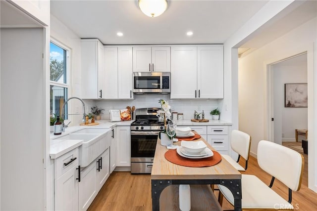 kitchen with white cabinetry, sink, stainless steel appliances, tasteful backsplash, and light hardwood / wood-style floors