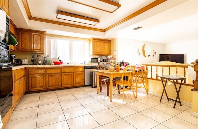 kitchen with tile countertops, dishwasher, ornamental molding, light tile patterned floors, and a tray ceiling