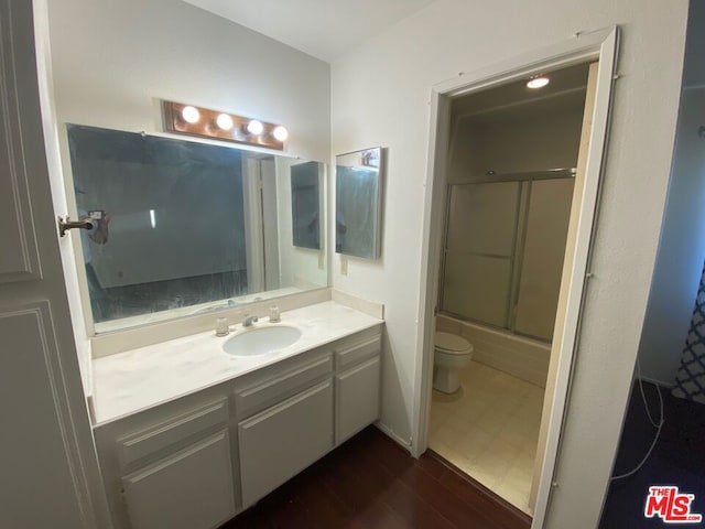 full bathroom featuring hardwood / wood-style flooring, combined bath / shower with glass door, toilet, and vanity