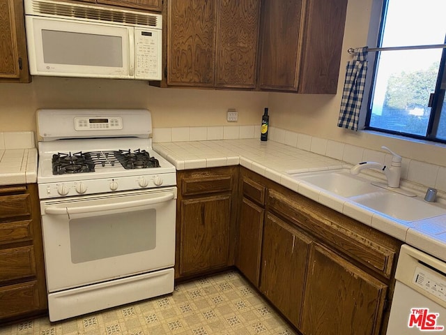 kitchen featuring white appliances, tile countertops, dark brown cabinetry, and sink