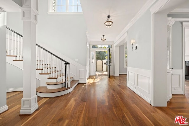 foyer entrance with crown molding, ornate columns, and dark wood-type flooring