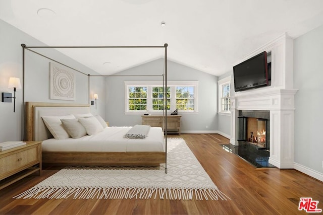 bedroom with a high end fireplace, lofted ceiling, and hardwood / wood-style flooring