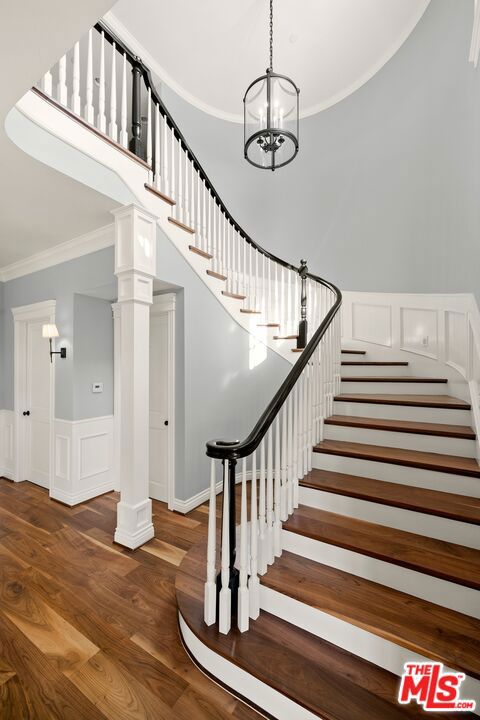 stairway featuring a chandelier, wood-type flooring, and ornamental molding