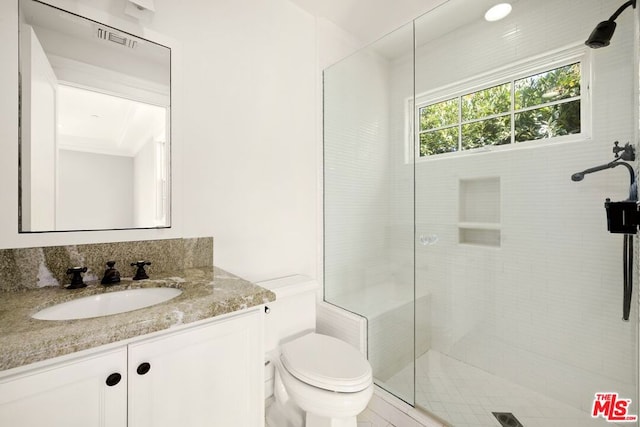 bathroom with a tile shower, vanity, and toilet