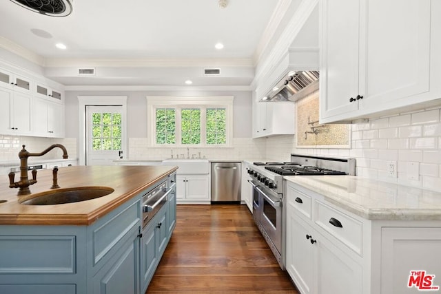 kitchen with wooden counters, appliances with stainless steel finishes, blue cabinets, sink, and white cabinetry