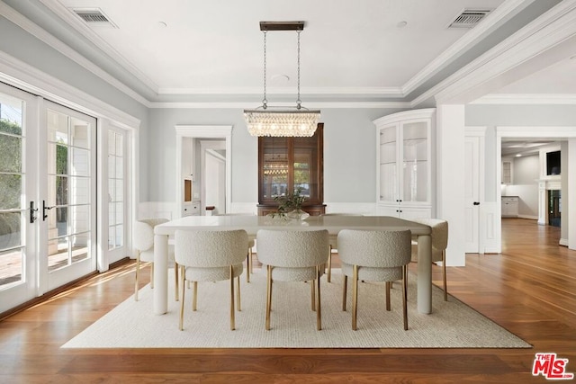 dining space featuring hardwood / wood-style flooring, french doors, crown molding, and a chandelier