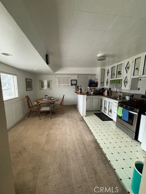 kitchen featuring light carpet, sink, white cabinetry, and stainless steel range with gas stovetop