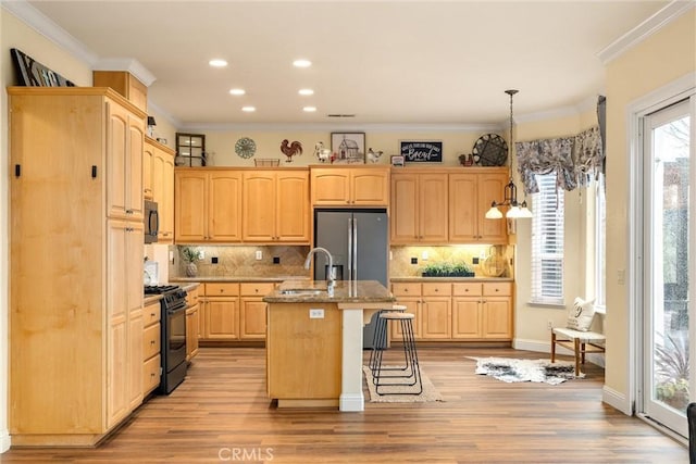 kitchen with black appliances, decorative light fixtures, light brown cabinetry, light wood-type flooring, and a center island with sink