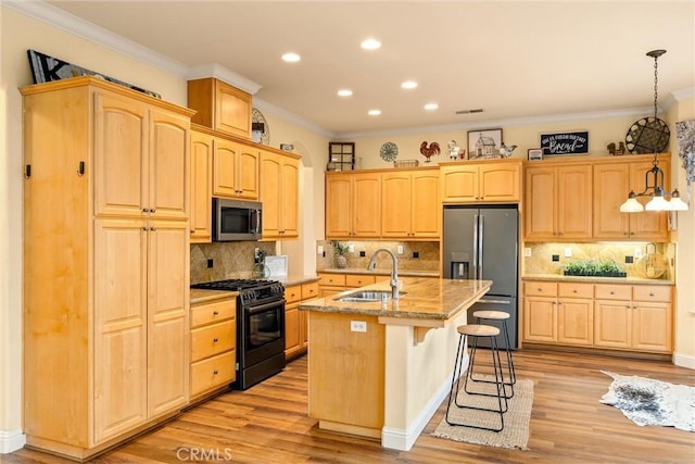 kitchen featuring appliances with stainless steel finishes, decorative light fixtures, a kitchen island with sink, light hardwood / wood-style flooring, and sink