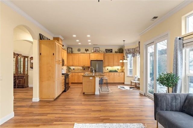 kitchen featuring a center island with sink, stainless steel refrigerator with ice dispenser, hanging light fixtures, a kitchen breakfast bar, and light brown cabinets