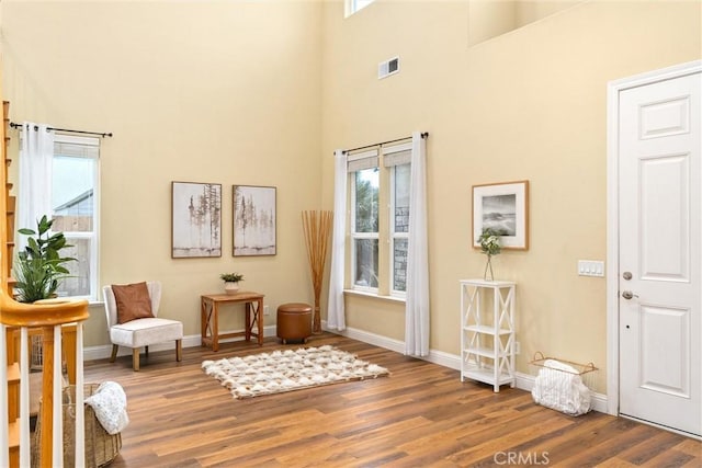 living area with a healthy amount of sunlight, a towering ceiling, and hardwood / wood-style floors