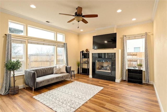 living room with ceiling fan, a tile fireplace, crown molding, and light hardwood / wood-style floors