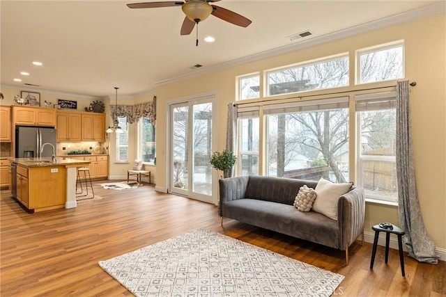 living room featuring ceiling fan, light hardwood / wood-style floors, sink, and ornamental molding