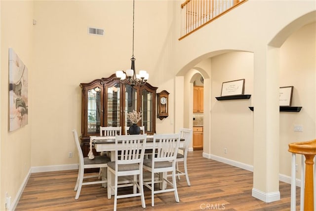 dining area with a high ceiling, hardwood / wood-style floors, and an inviting chandelier