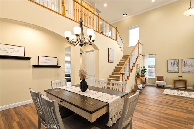 dining area featuring a towering ceiling, a wealth of natural light, dark hardwood / wood-style floors, and a chandelier