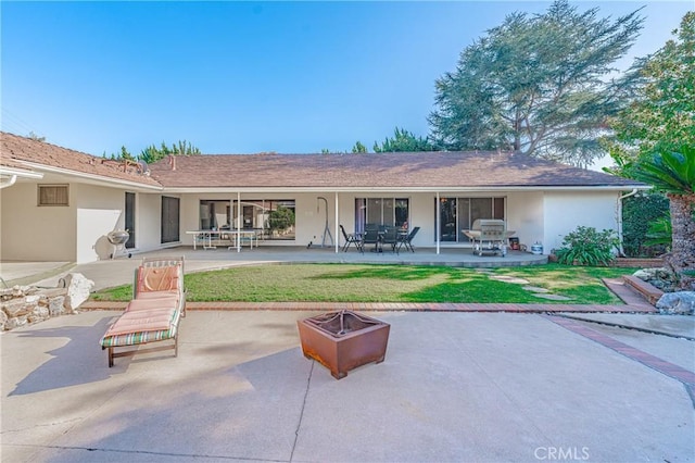 back of house featuring a lawn, a patio, and a fire pit