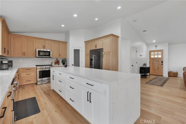 kitchen featuring light hardwood / wood-style floors, a center island with sink, appliances with stainless steel finishes, vaulted ceiling, and white cabinets