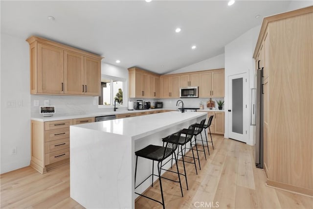 kitchen featuring an island with sink, appliances with stainless steel finishes, tasteful backsplash, light hardwood / wood-style flooring, and a breakfast bar