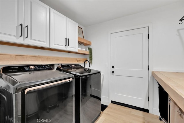 washroom with washer and clothes dryer, light hardwood / wood-style floors, and cabinets