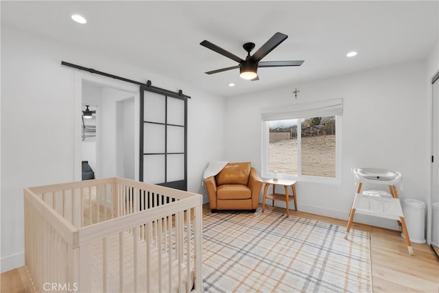 bedroom featuring ceiling fan, wood-type flooring, a barn door, and a nursery area